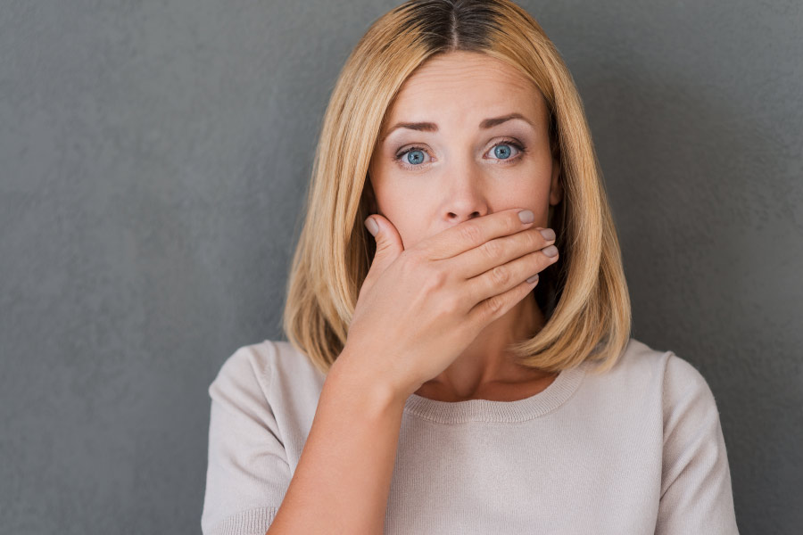 Blonde woman covering her mouth to hide her bad breath.