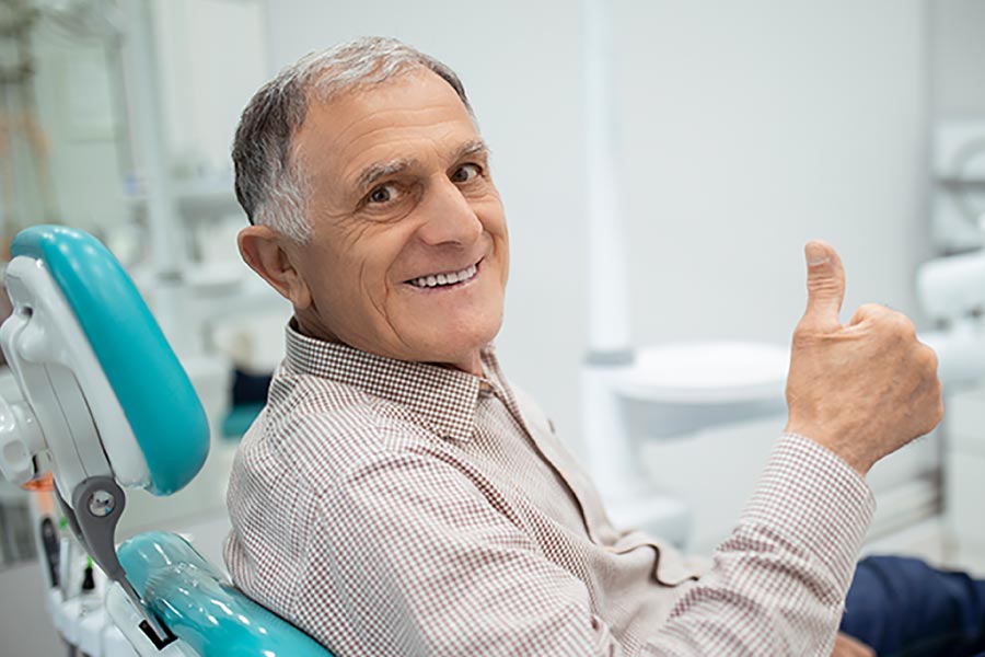Gray haired gentleman give the thumbs up sign from the dental chair.