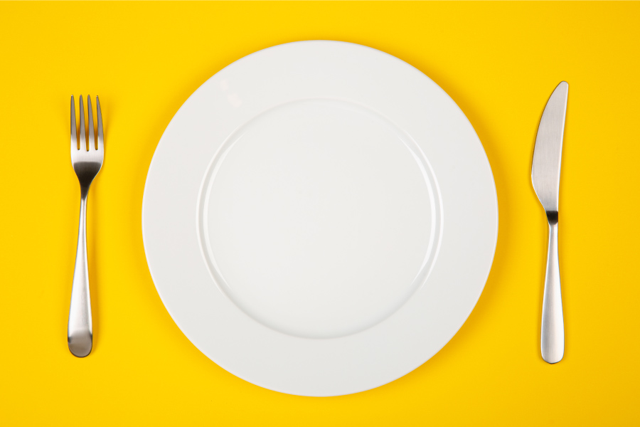 Aerial view of a white plate against a yellow table with a fork and knife