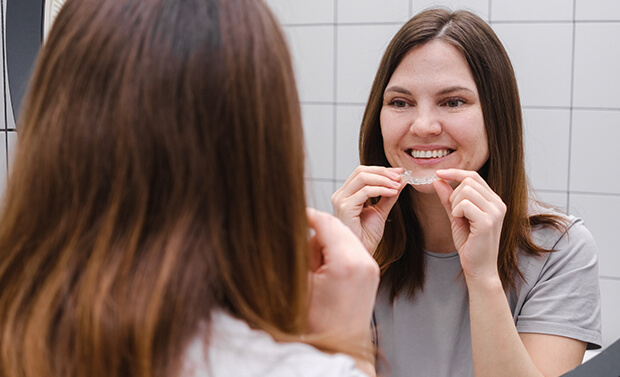 woman inserting a clear aligner onto her teeth