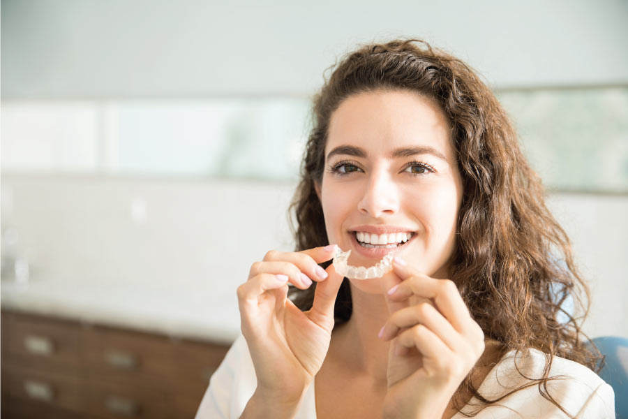 woman smiles as she insert her clear aligner to straighten teeth