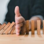 preventive dental care shown by hand holding up wooden dominoes, skipping dental visits can cost more money in the long run