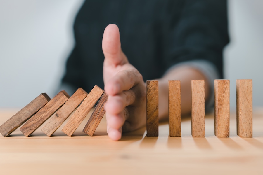 preventive dental care shown by hand holding up wooden dominoes, skipping dental visits can cost more money in the long run